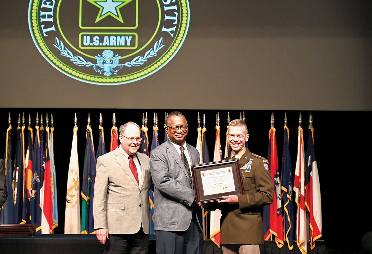 Dwayne K. Wagner from the Department of Joint, Interagency and Multinational Operations in the Command and General Staff School, center, receives his Silver Pen Award during the faculty awards ceremony in the Lewis and Clark Center on April 4, 2022, from CGSC Dean of Academics Dr. Jack Kemp, left, and CGSC Deputy Commandant Maj. Gen. Donn H. Hill. Wagner is a member of the CGSC Foundation board of trustees.
