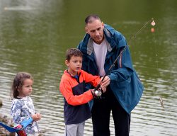 Argentine Maj. Ezequiel Gonzales, Command and General Staff Officer Course student, explains how to hold a fishing rod to his children, 7-year-old Cristobal and 4-year-old Amaparo, as they reel in a fish during the second annual International Families Fishing Derby Sept. 10, 2022, at Merritt Lake. (Photo by Charlotte Richter/Fort Leavenworth Lamp)