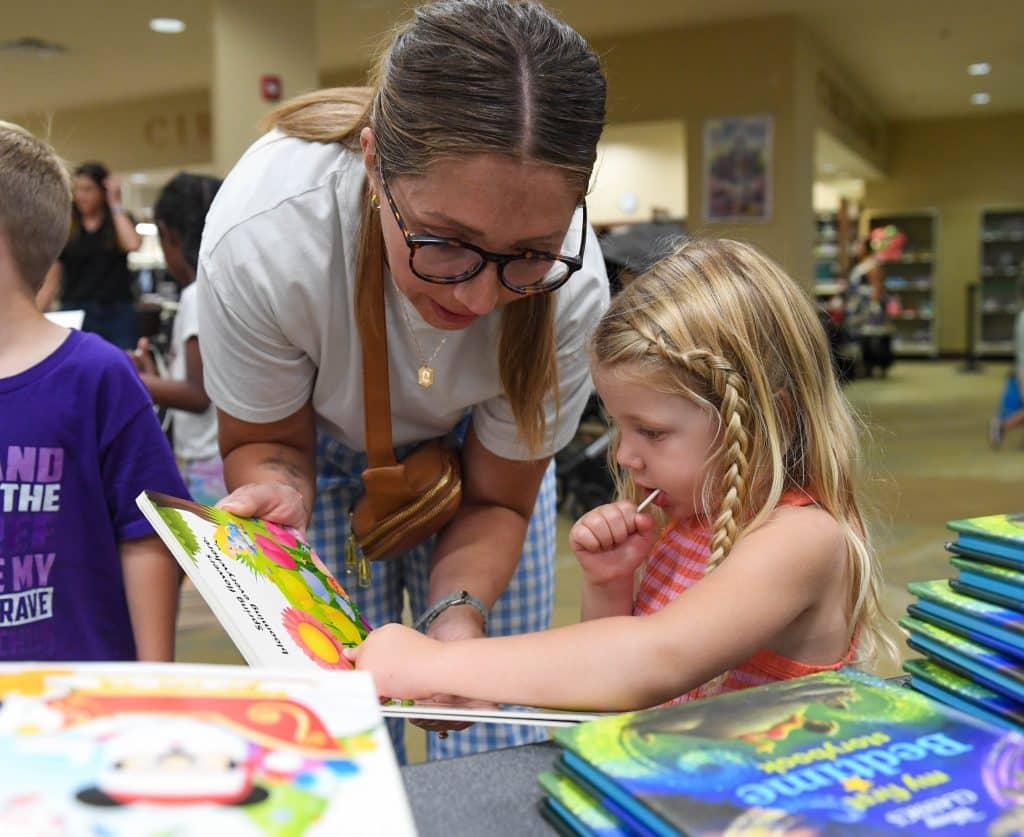 A child and their mother look at board books at the "Check-out Your Library" book giveaway on Aug. 1, 2025.